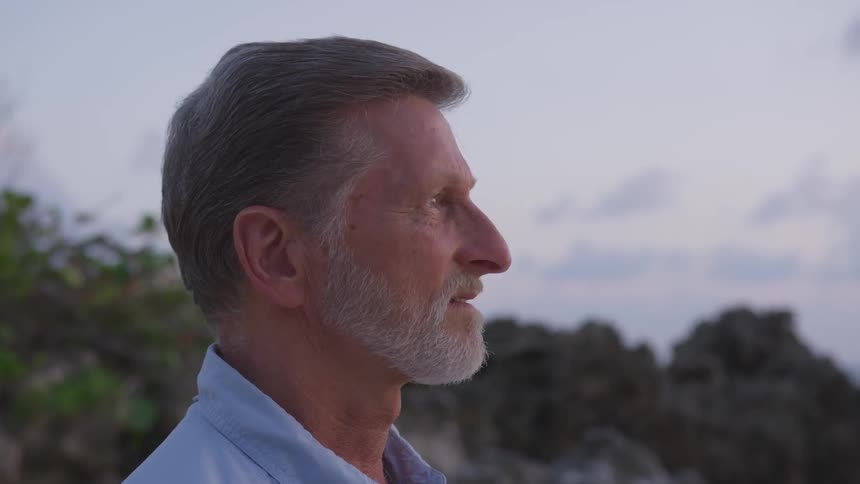 Man with blue shirt and gray beard looking straight ahead