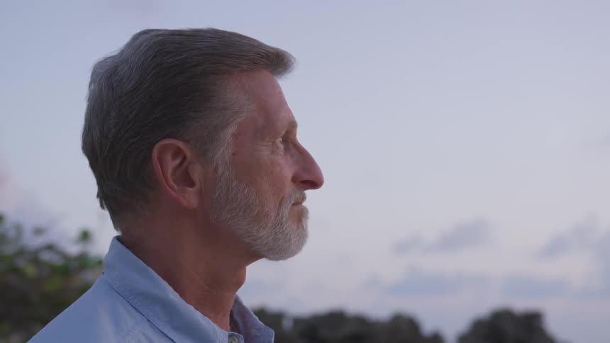 Bearded old man wearing blue shirt looks ahead in the forest at dusk