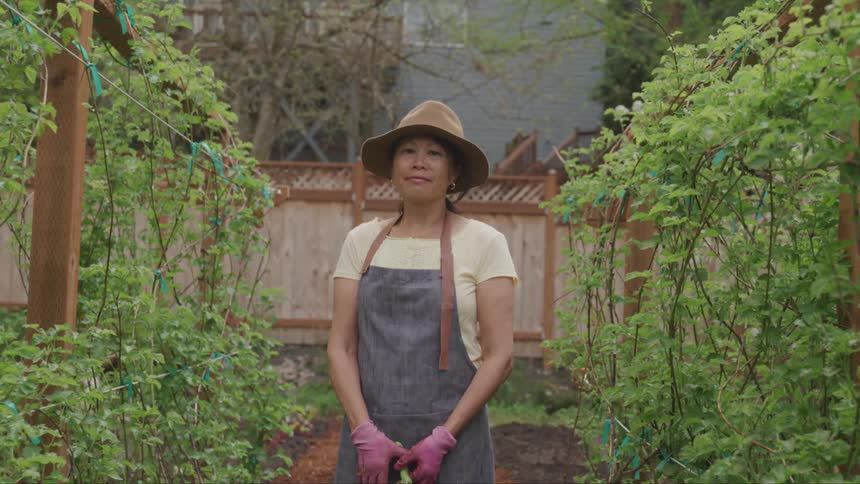 A woman in an apron and hat standing in her garden