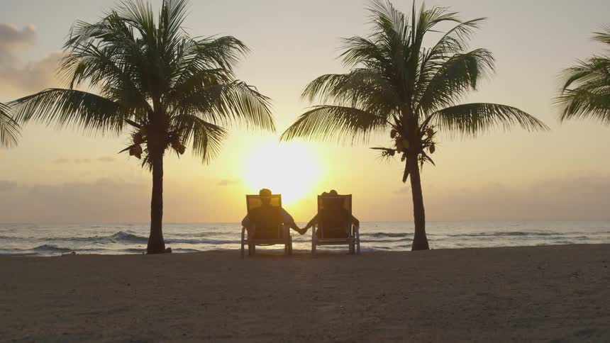 A couple hold hands while looking at a sunset on a beach