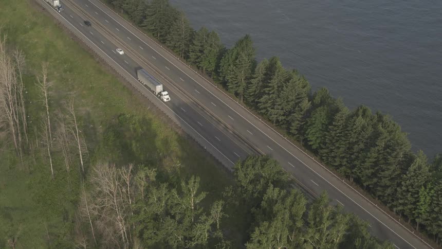 Traffic drives down a four lane highway next to a body of water