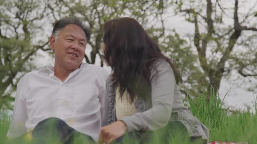 A man and woman smile while sitting and talking in a grassy field