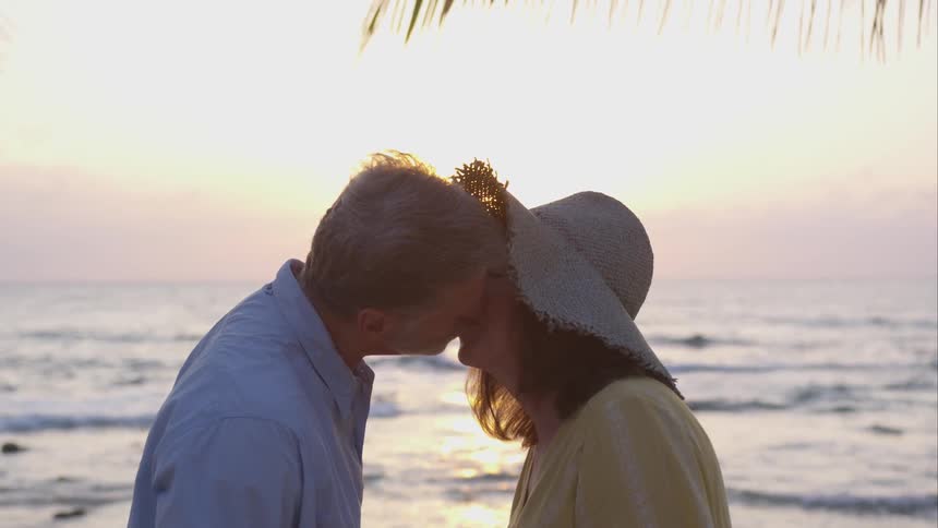 A man and woman lean in to kiss by the ocean coast line