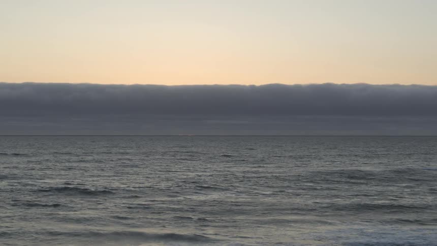 A bank of thick clouds looms of the horizon over the open ocean as waves gently roll across the surface of the water