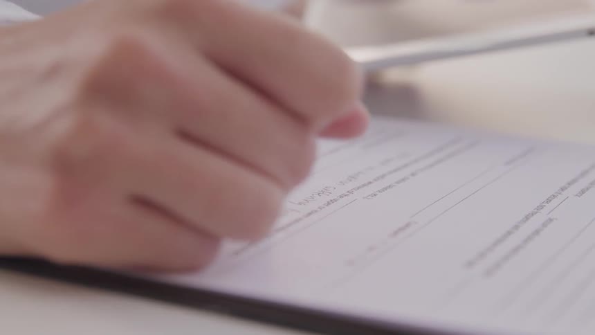 A person writes on paper while looking at something on a tablet