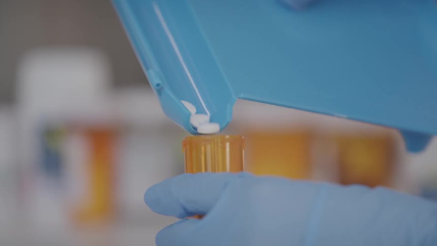 A person with blue gloves pours pills into an orange bottle in a pharmacy