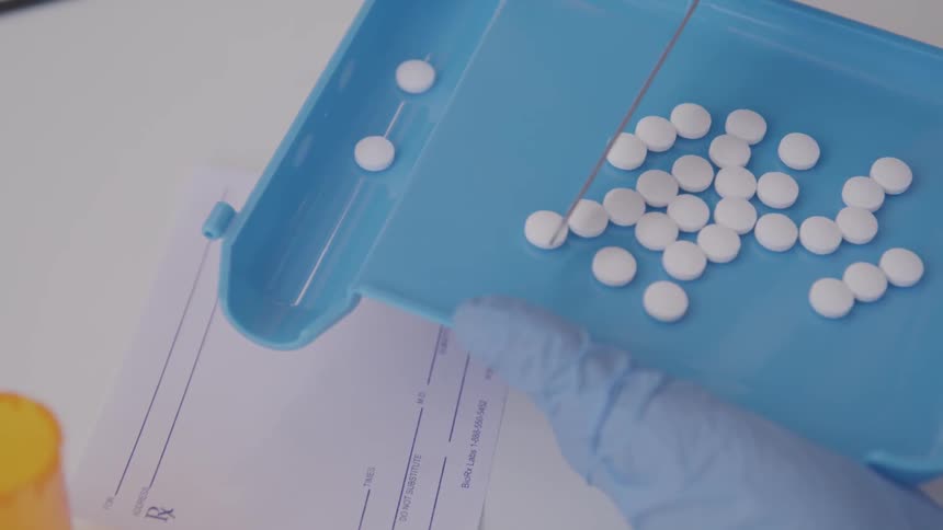 Pills are counted from a tray into a shoot by a pharmacist