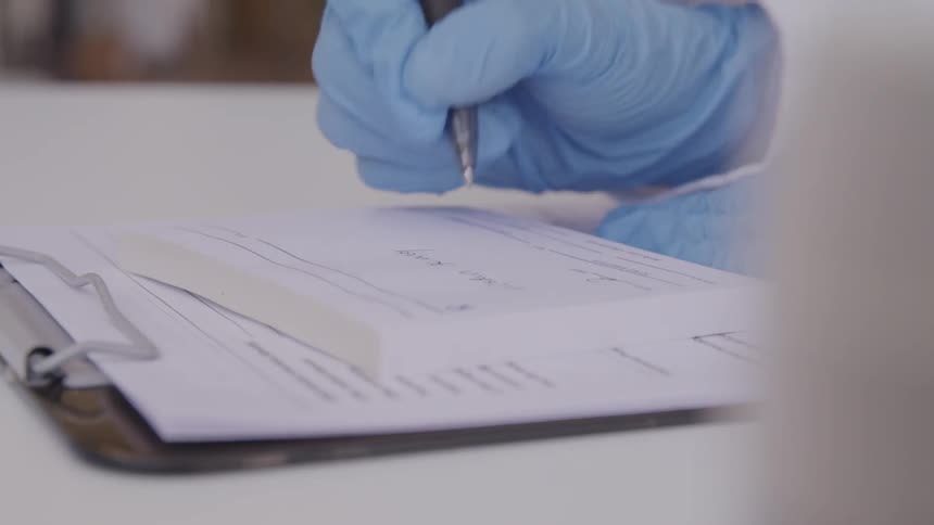Hand in blue glove holding ballpoint pen is writing on a prescription sheet
