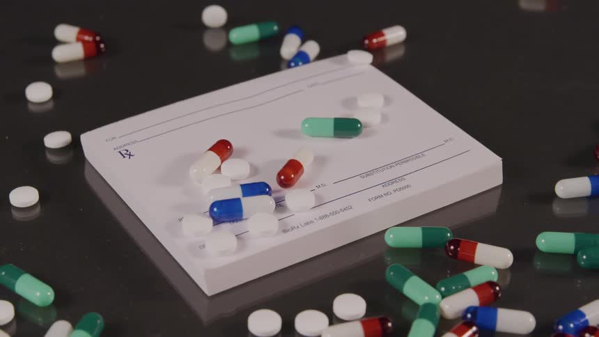 A range of pills are dropped onto a notepad on a desk