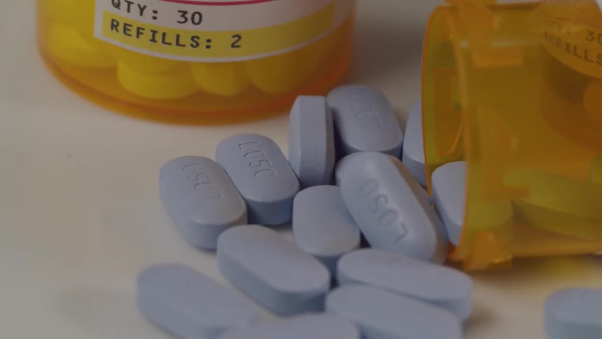 Oblong blue pills spilling out of a pill bottle lying on its side beside a second bottle of pills