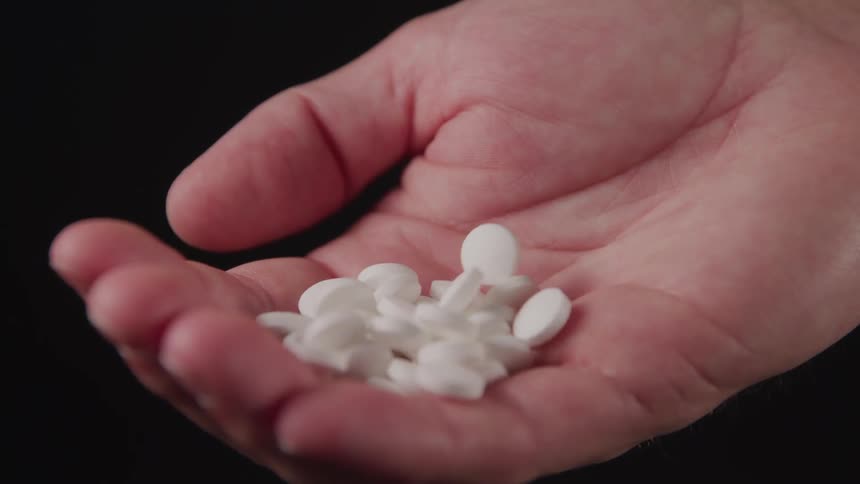 Pills fall into the open palm of the man on the black background