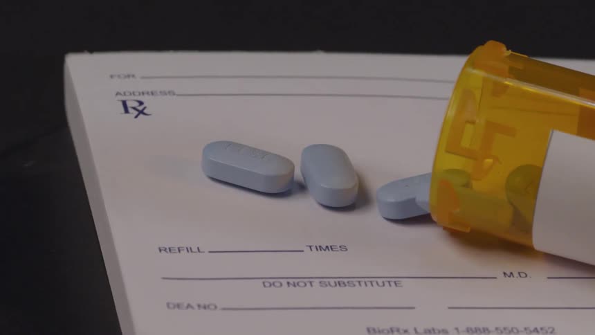 Blue pills spill out from a pill bottle onto a prescription pad