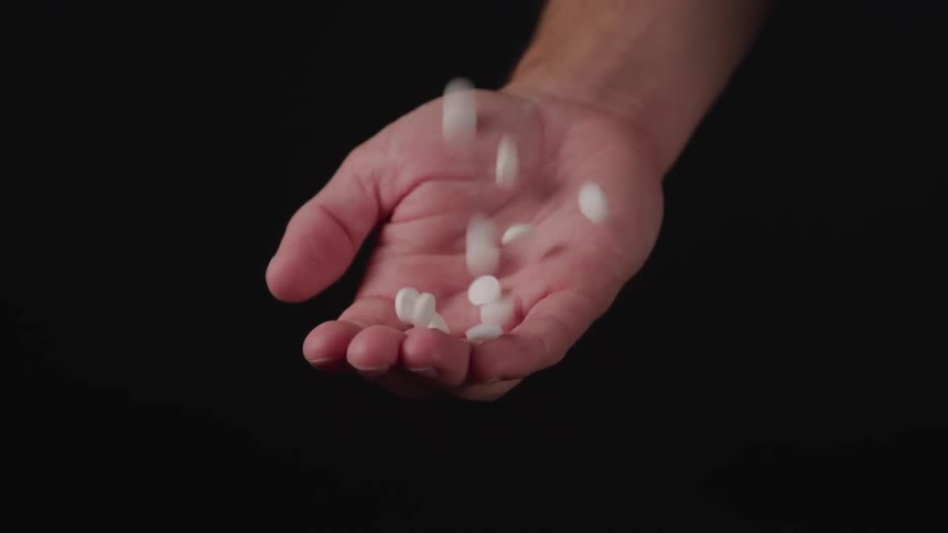 Pills fall into the open palm of the man on the black background