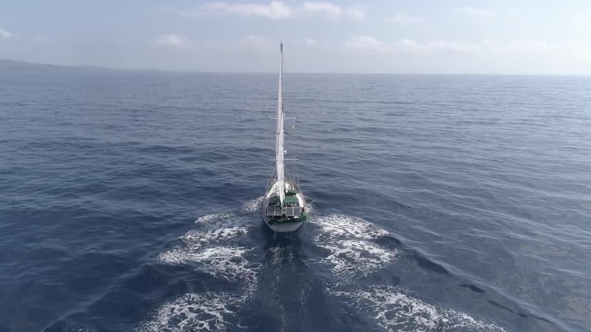 A sailboat in the middle of the ocean with the sky and clouds in the background