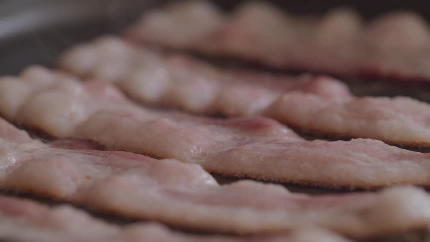 A row of bacon strips frying on a pan