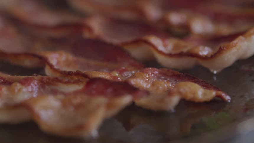 Grease bubbles on strips of bacon frying on a pan