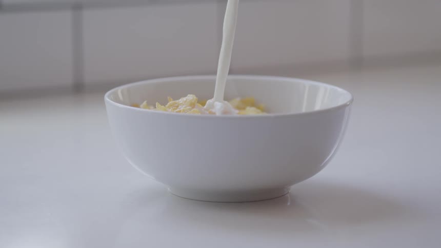 Milk is being poured in to a bowl of cereal