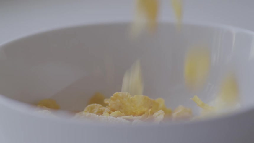 Corn flakes fall into a white ceramic bowl