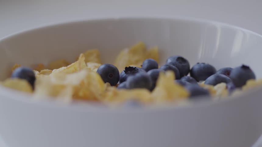 Blueberries dropping into a bowl of cereal
