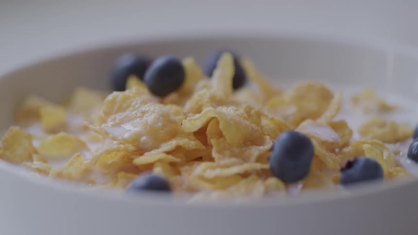 Blueberries dropping into a bowl of cornflakes