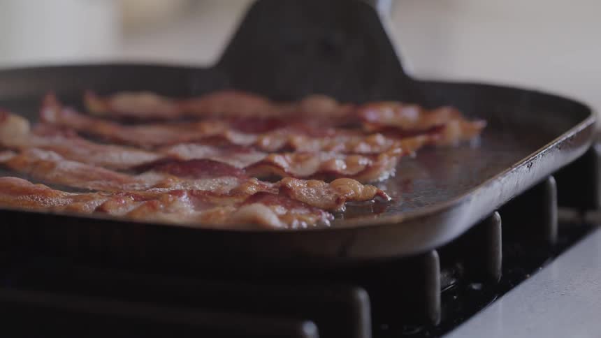 Strips of bacon cook on a griddle on a stove top