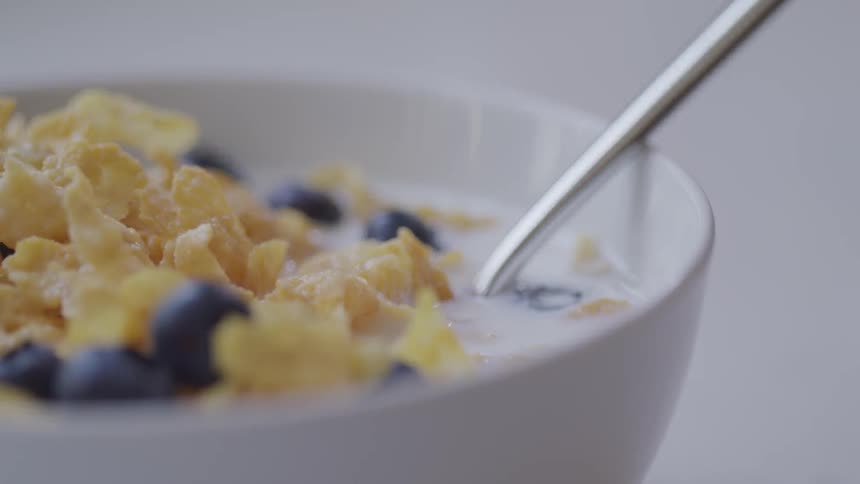 Bowl of cornflakes blueberries and milk with a spoon