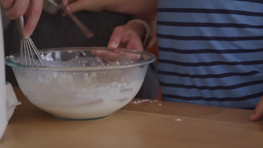 People whisk a mixture together in a mixing bowl