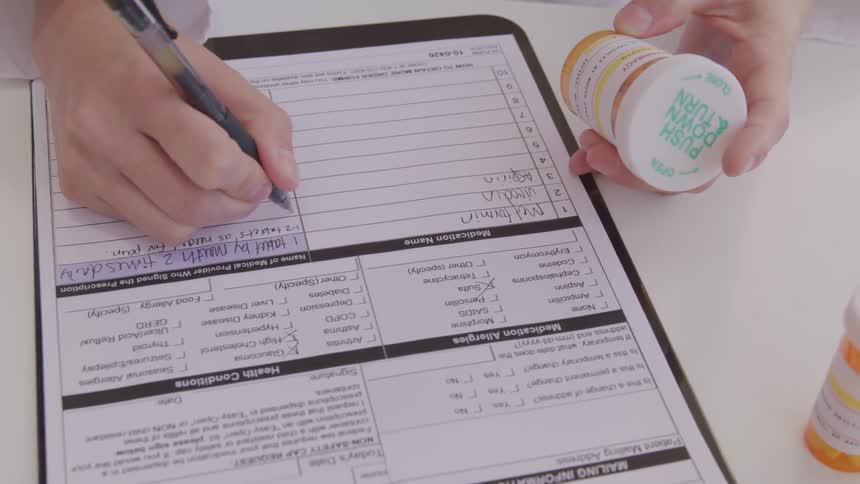 A person holds a prescription bottle and writes on a piece of paper