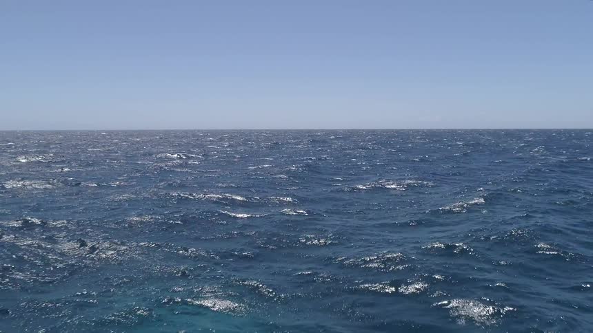 Waves roll across the ocean under a blue sky