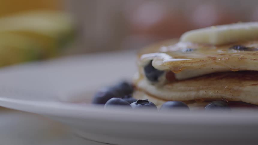 Syrup dripping from blueberry pancakes on a white plate
