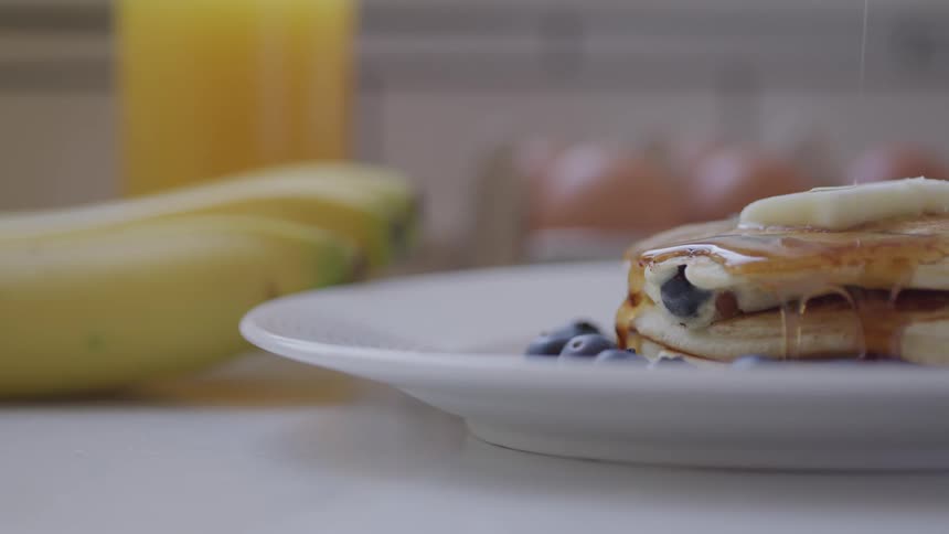 Maple syrup is poured on blueberry pancakes