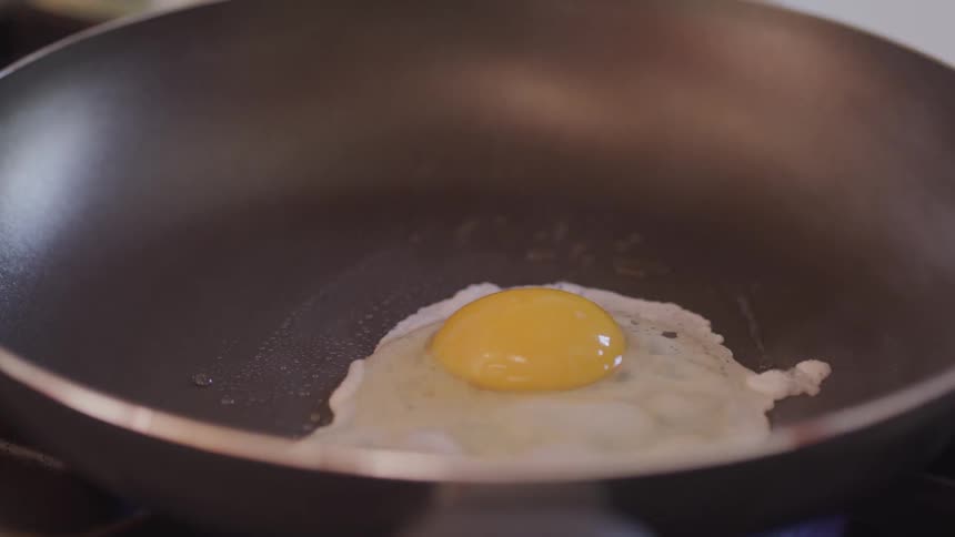 A womans hand cracking a egg into a frying pan
