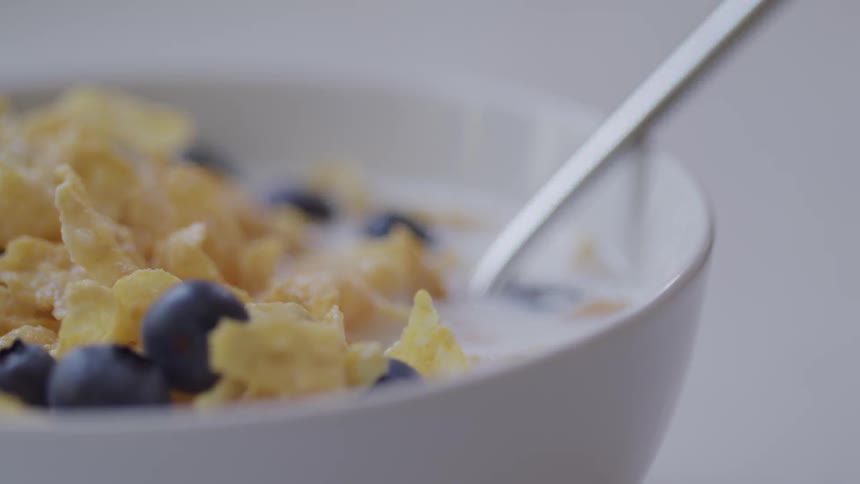 A metal spoon rests in a bowl of cereal and blueberries