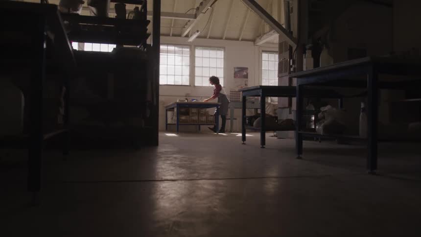 A person leaning over a work table in a large warehouse type room