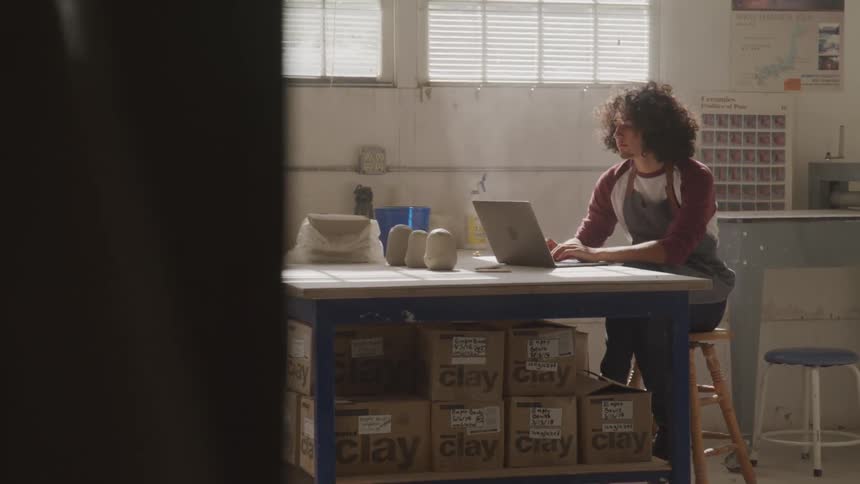 Long hair man sits at the table and uses laptop indoors during daylight