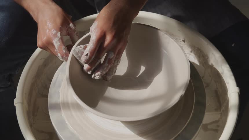 Man spinning a clay vase on a pottery wheel