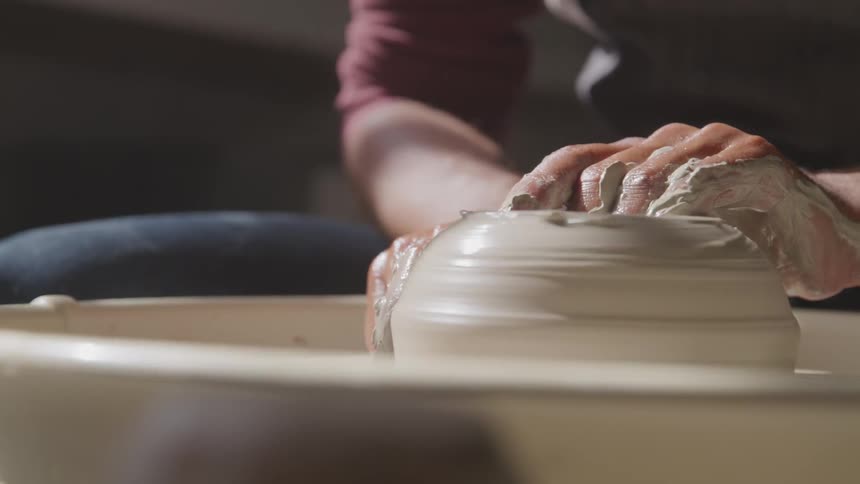 A person uses their hand to form clay on a pottery wheel