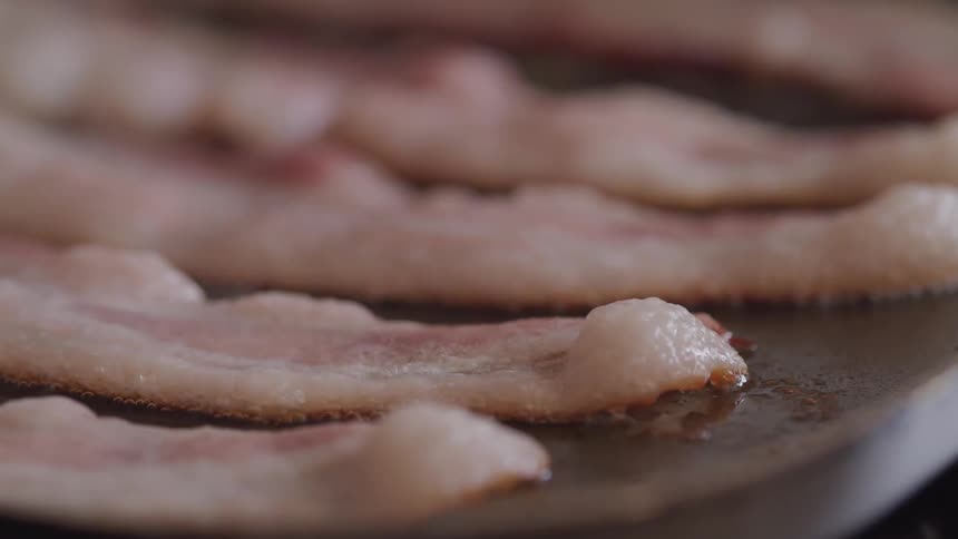 Bacon strips on a griddle sizzle and lift as they cook