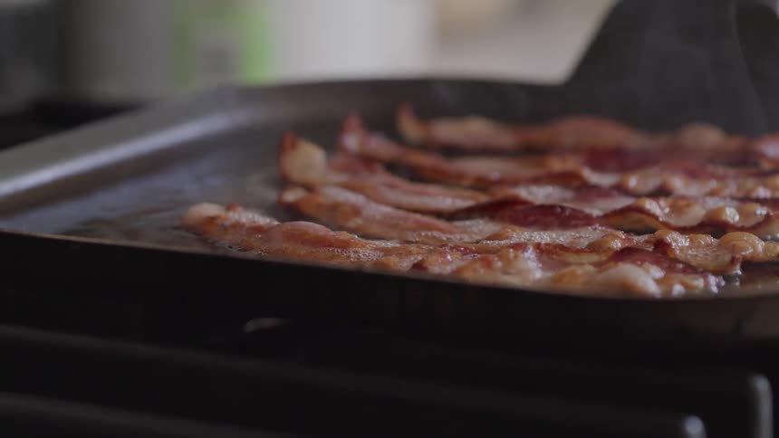 Bacon slices sizzle on a griddle