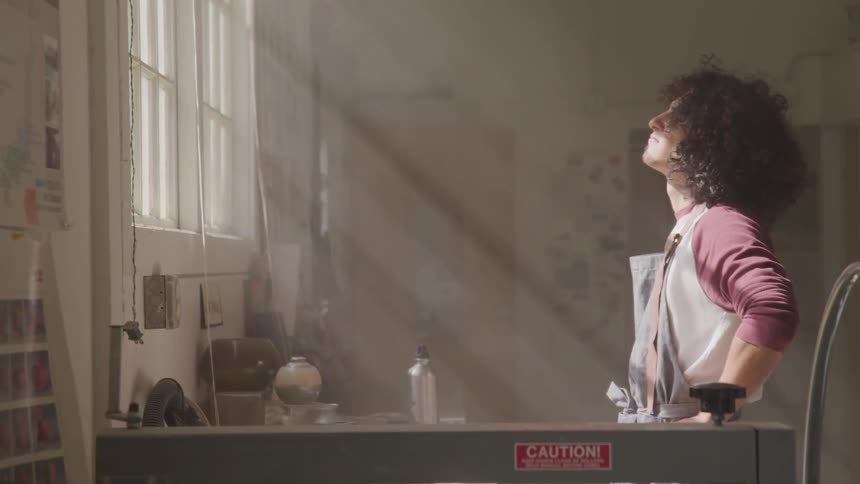 A man surrounded by tools stares out a large window