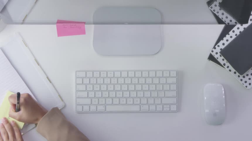 A woman writes a note on a yellow post it and sticks it on the bottom of her large monitor