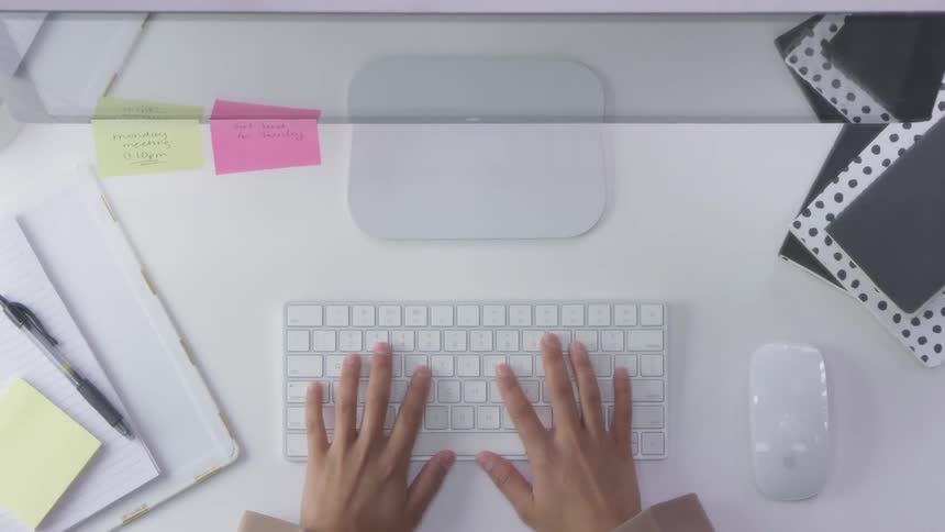 A person typing on a keyboard before keeping upset and shoving folders and notebooks off the desk