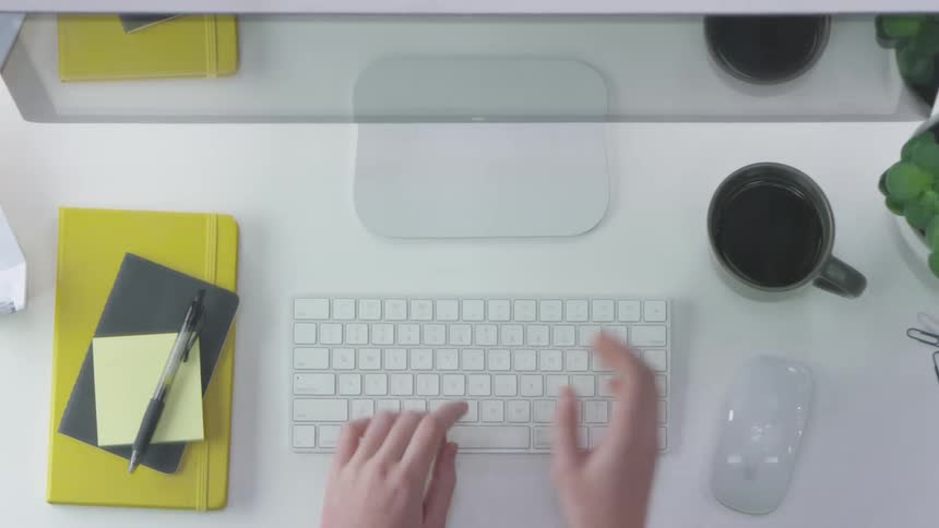 A woman types on a keyboard and picks up a mug
