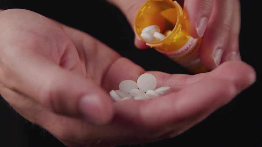 Circular pills poured from a pharmaceutical bottle into a hand which is then clenched and raised