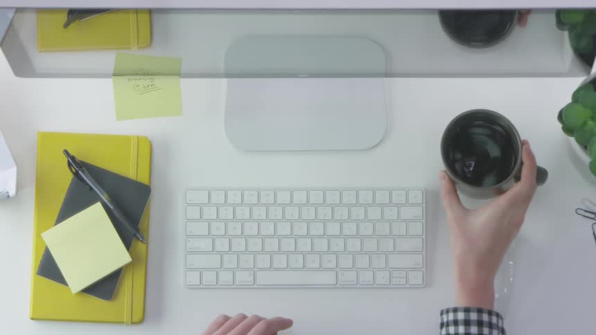 A person grabs a cup of coffee while working in front of a computer