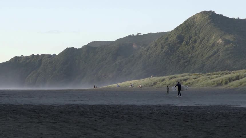 A wide view of a sandy beach stretching toward the ocean horizon, with gentle waves rolling in.
