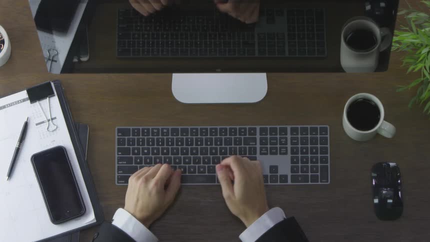 A person types quickly on a keyboard in front of a monitor and then suddenly slams their fist on the desk which causes the mug full of coffee to shake