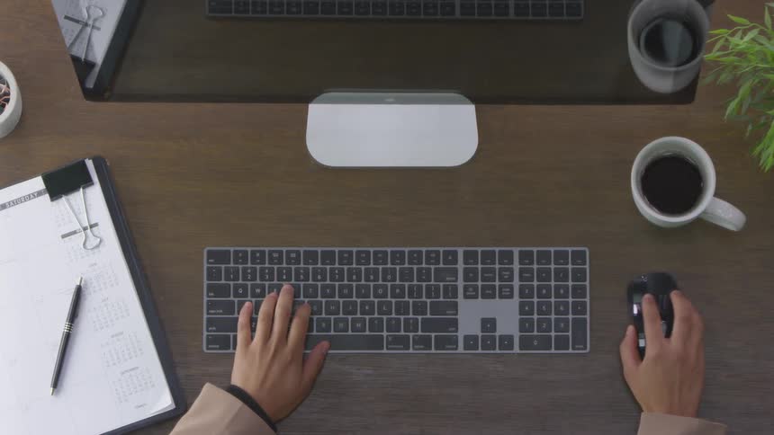 A man is typing on a gray keyboard uses his mouse briefly resumes typing and then takes his hands away