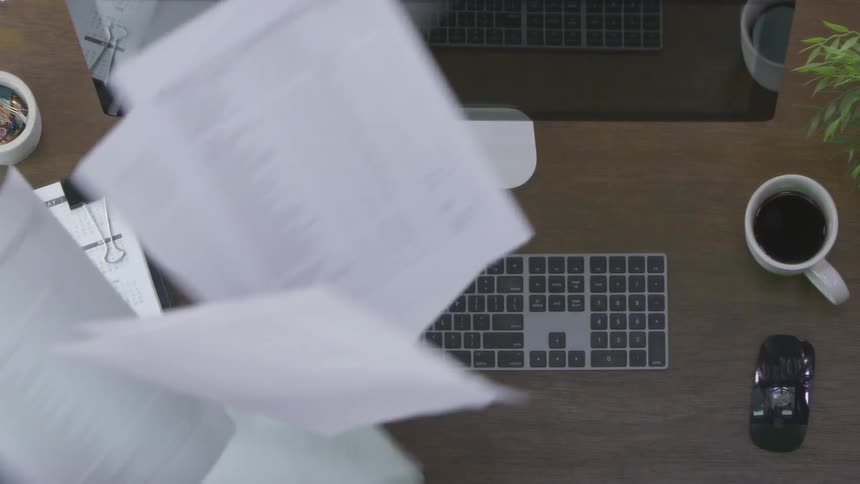 A person throws papers in the air in front of a computer
