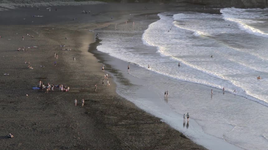 People wade or swim in the water while others relax on the beach